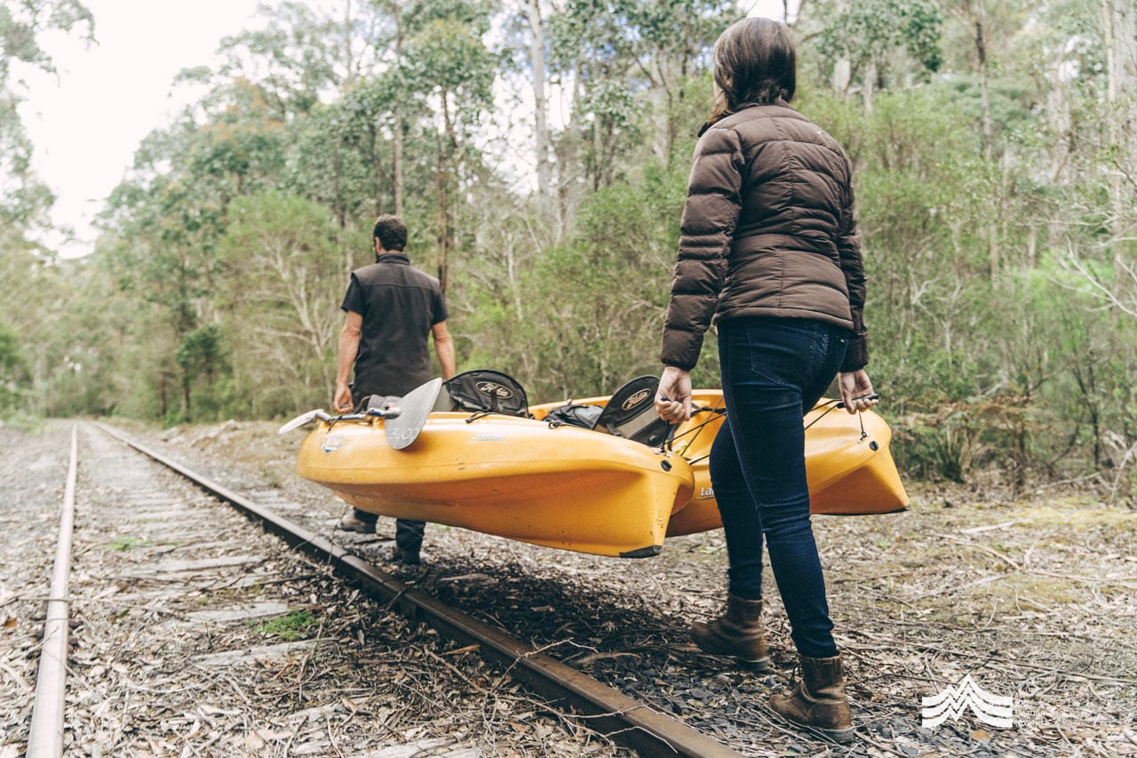 Liam and Fiona from Tassie Bound tours carrying a kayak along the railway track to the river